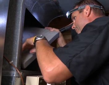 A person replacing an air filter in a ventilation system. They wear a headlamp.