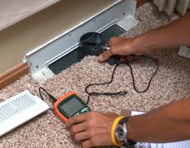 Person using a meter to inspect a floor vent, testing for something.