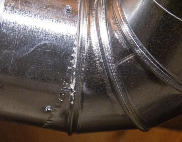 Metallic ductwork elbow with crimped seams and rivets.