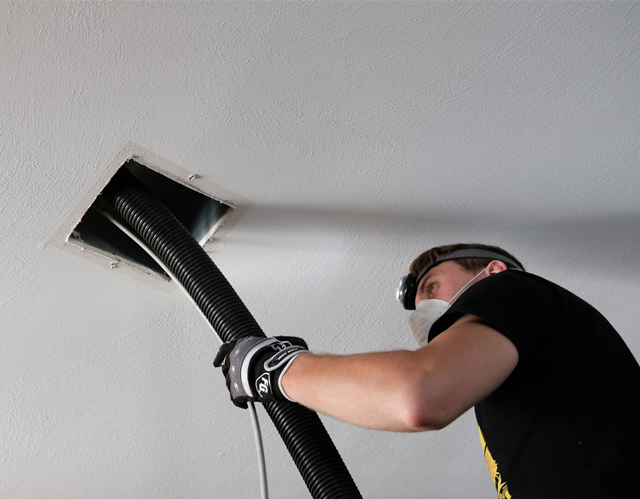 Person cleaning a ceiling air vent with a vacuum hose.