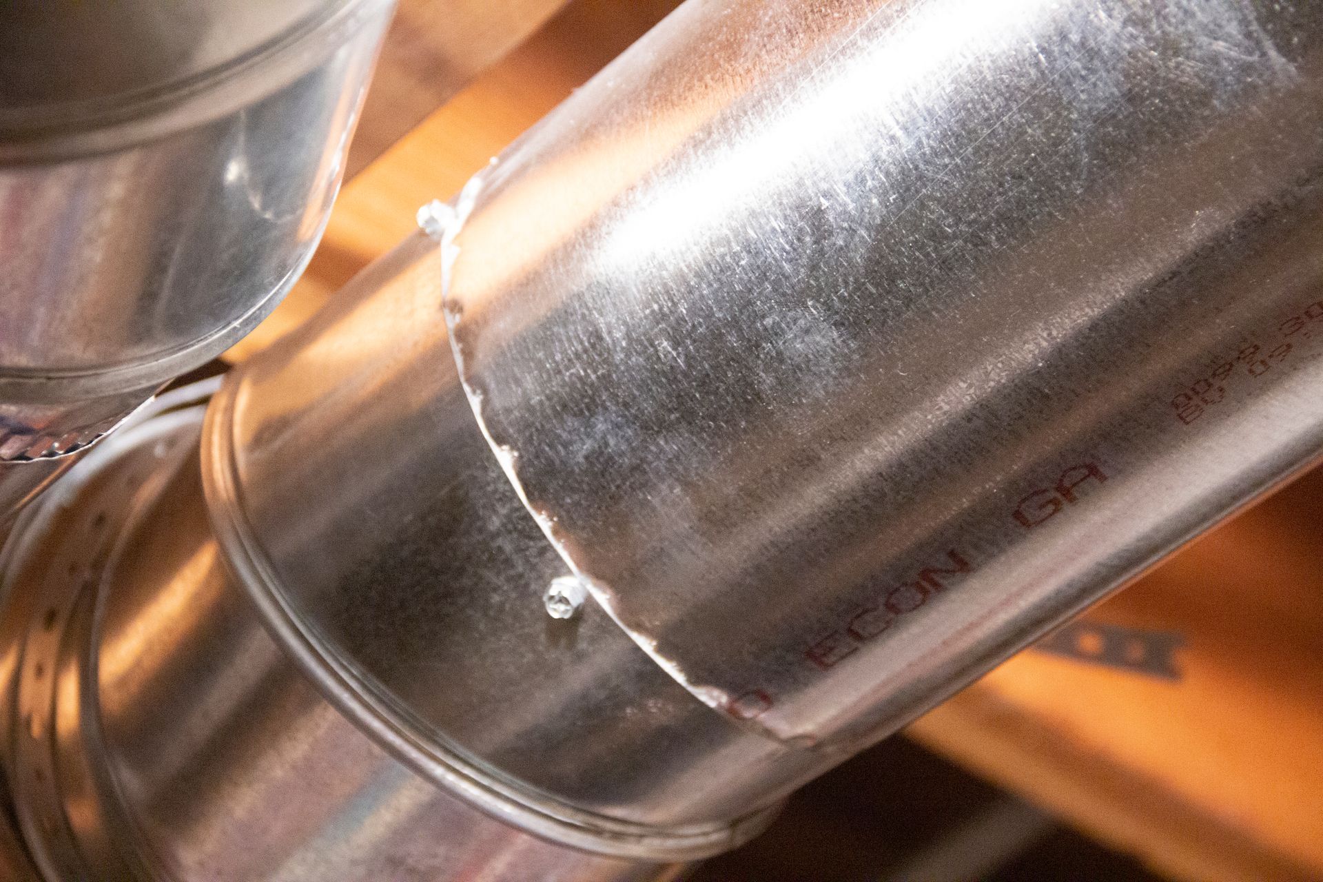 Metal ductwork with a visible seam and screw in an attic setting.