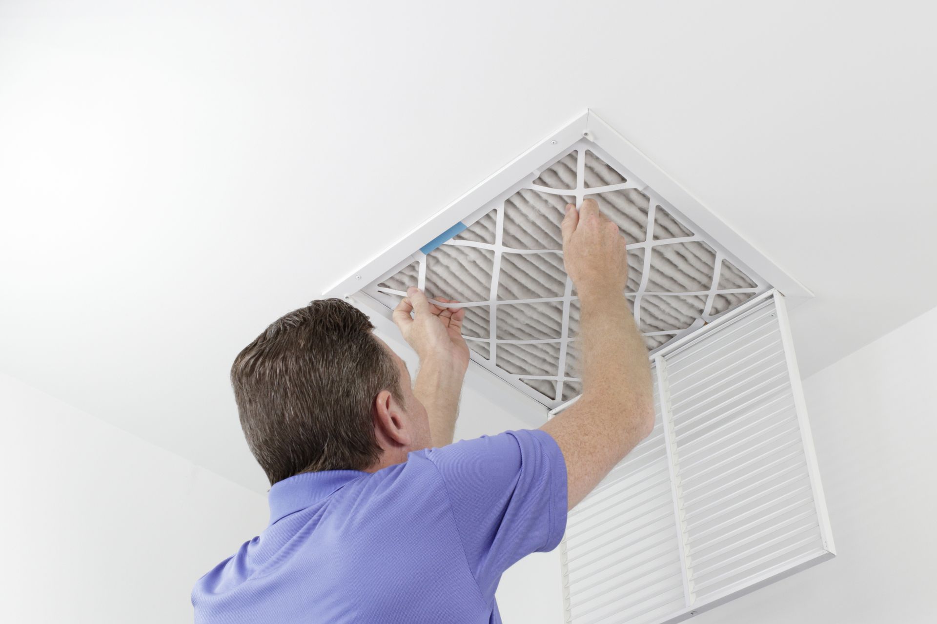 Person replacing air filter in ceiling vent.