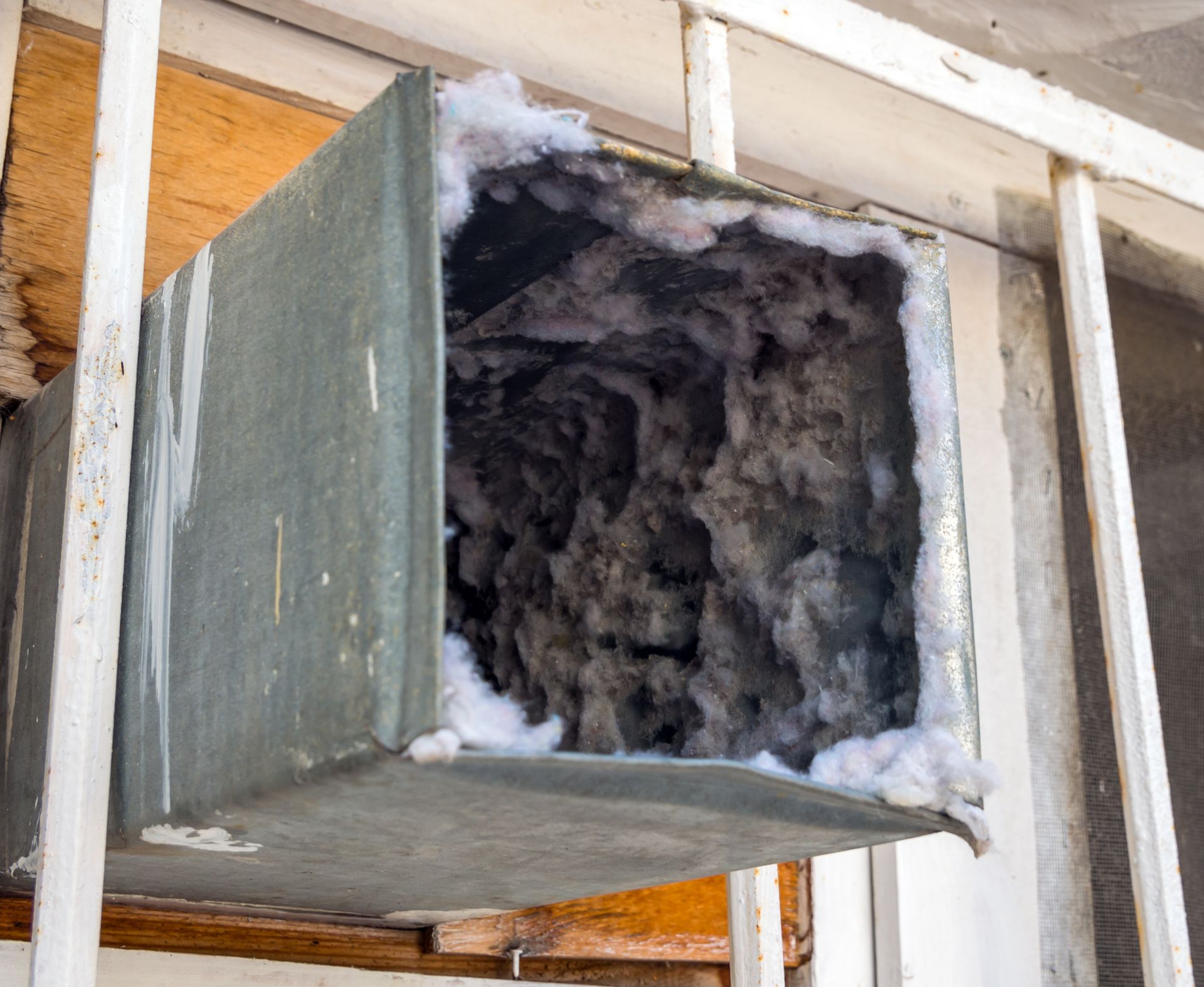 Dust-filled rectangular HVAC duct, silver metal, open end revealing thick layer of accumulated dust, mounted near a window.