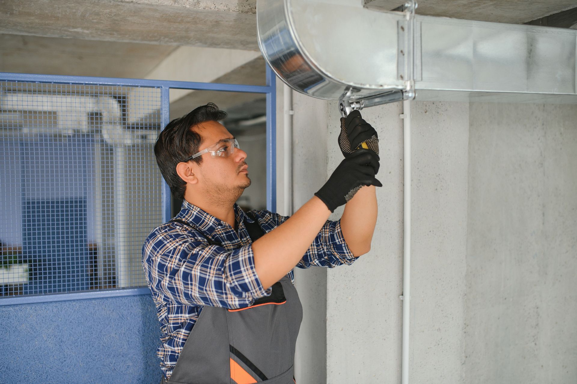 Man in work clothes and safety glasses works on HVAC ductwork in a workshop.