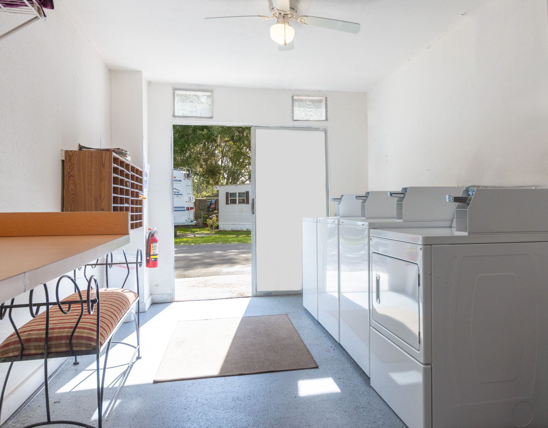 Laundry room with white appliances, open door to outdoors, bench with cushion.