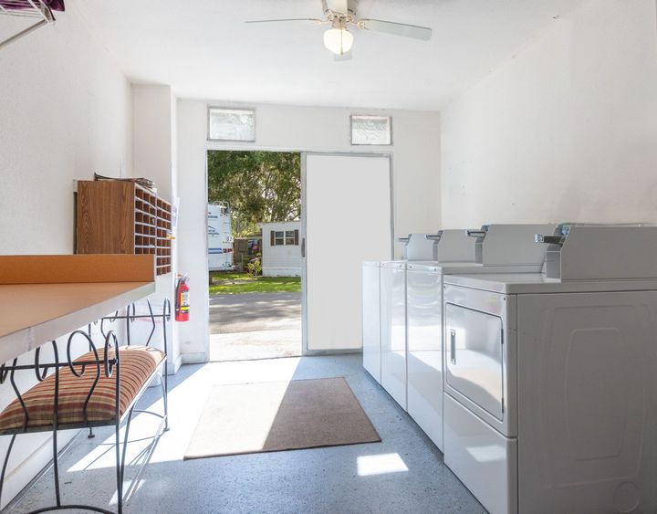 Laundry room with white appliances, open door to outdoors, bench with cushion.