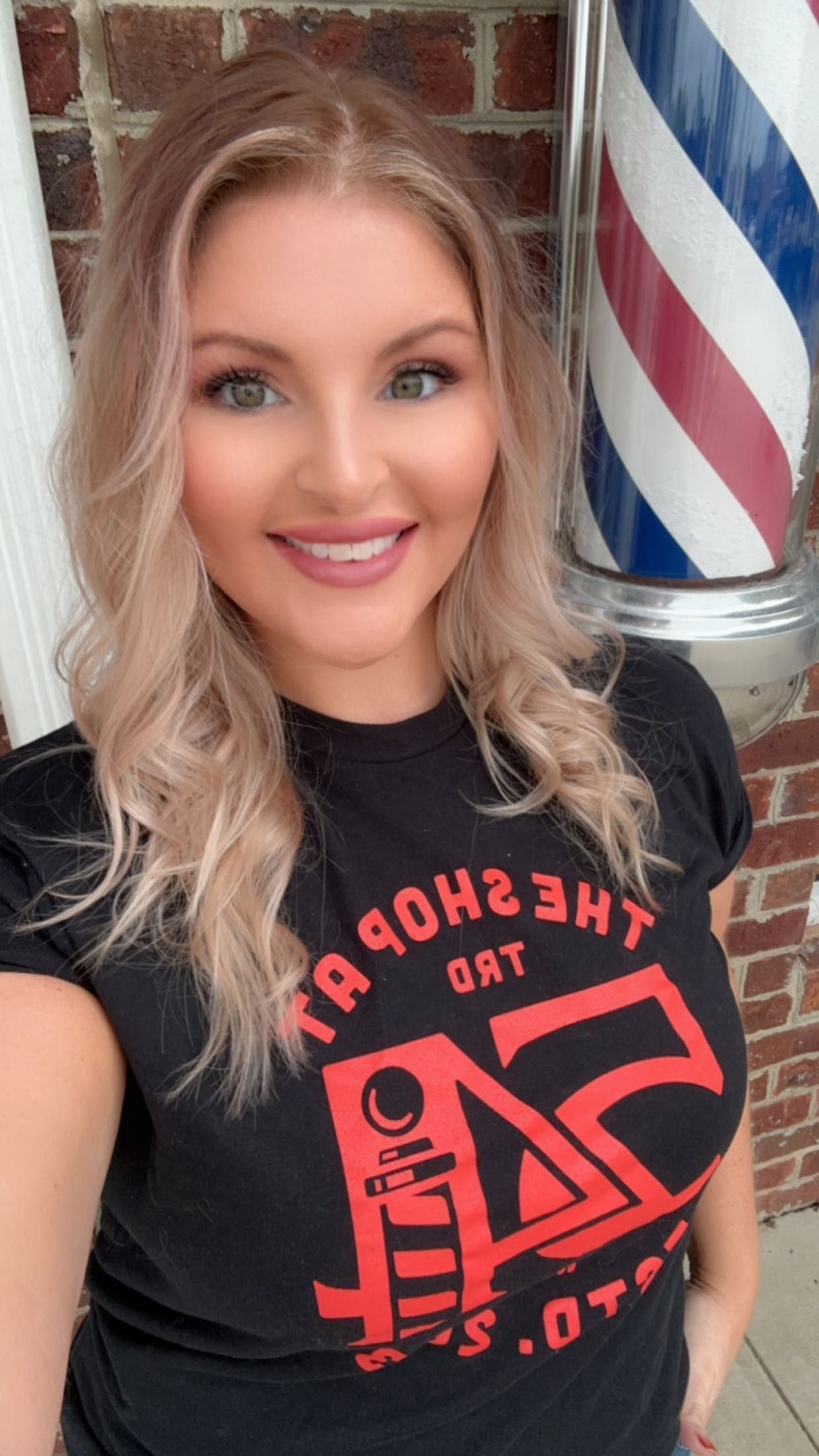 A woman in a black shirt is smiling in front of a barbershop pole.
