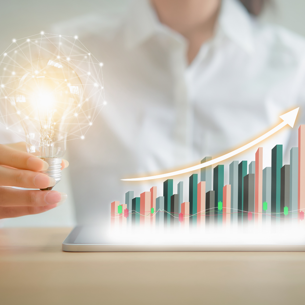 Hand holding glowing bulb beside rising bar chart and upward arrow on a tablet