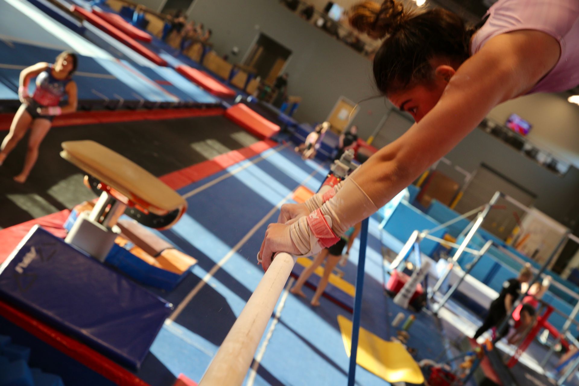 Gymnast mid-vault over the pommel horse in a colorful indoor gymnastics gym