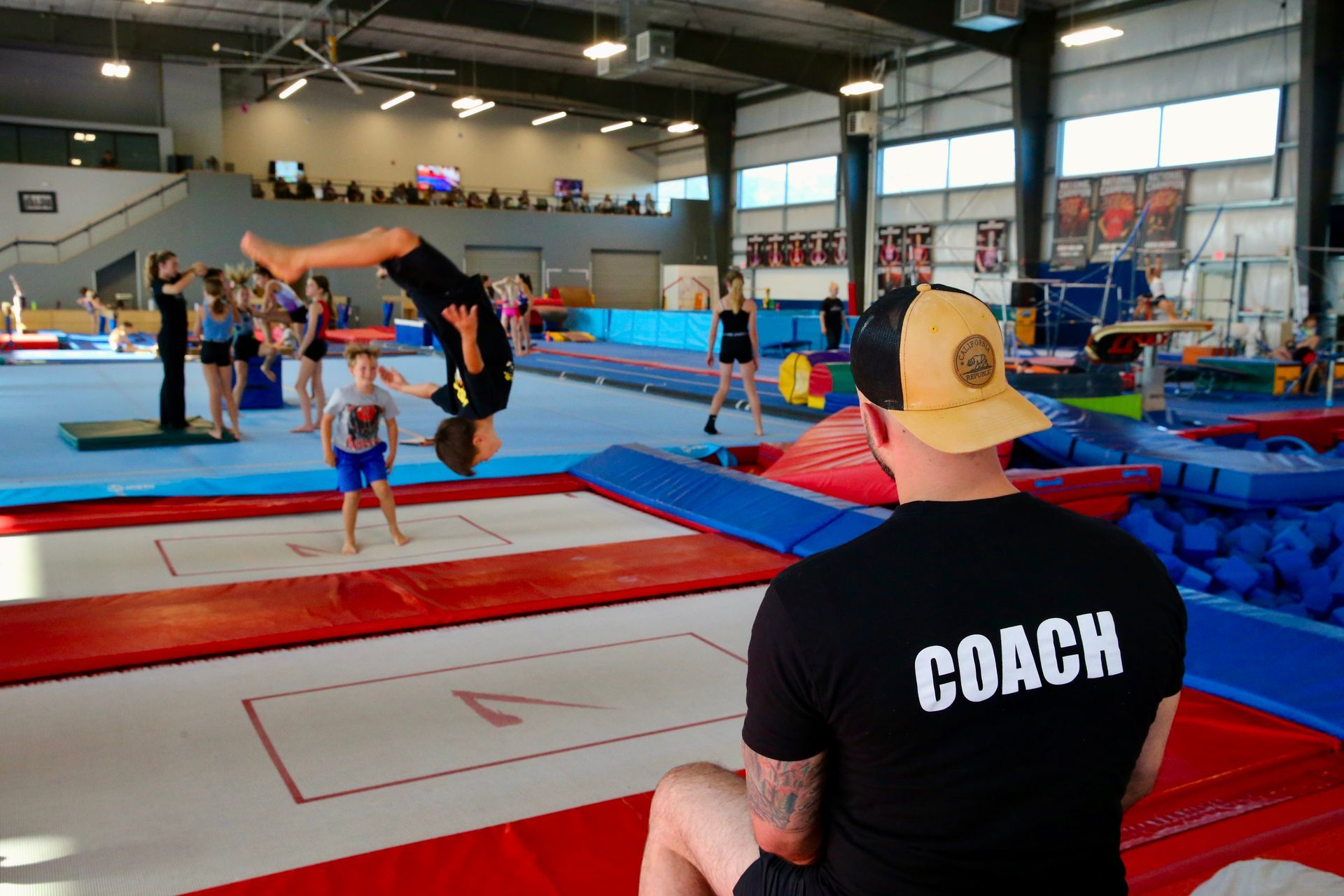 Coach watches gymnast flip on trampoline in indoor gym training area
