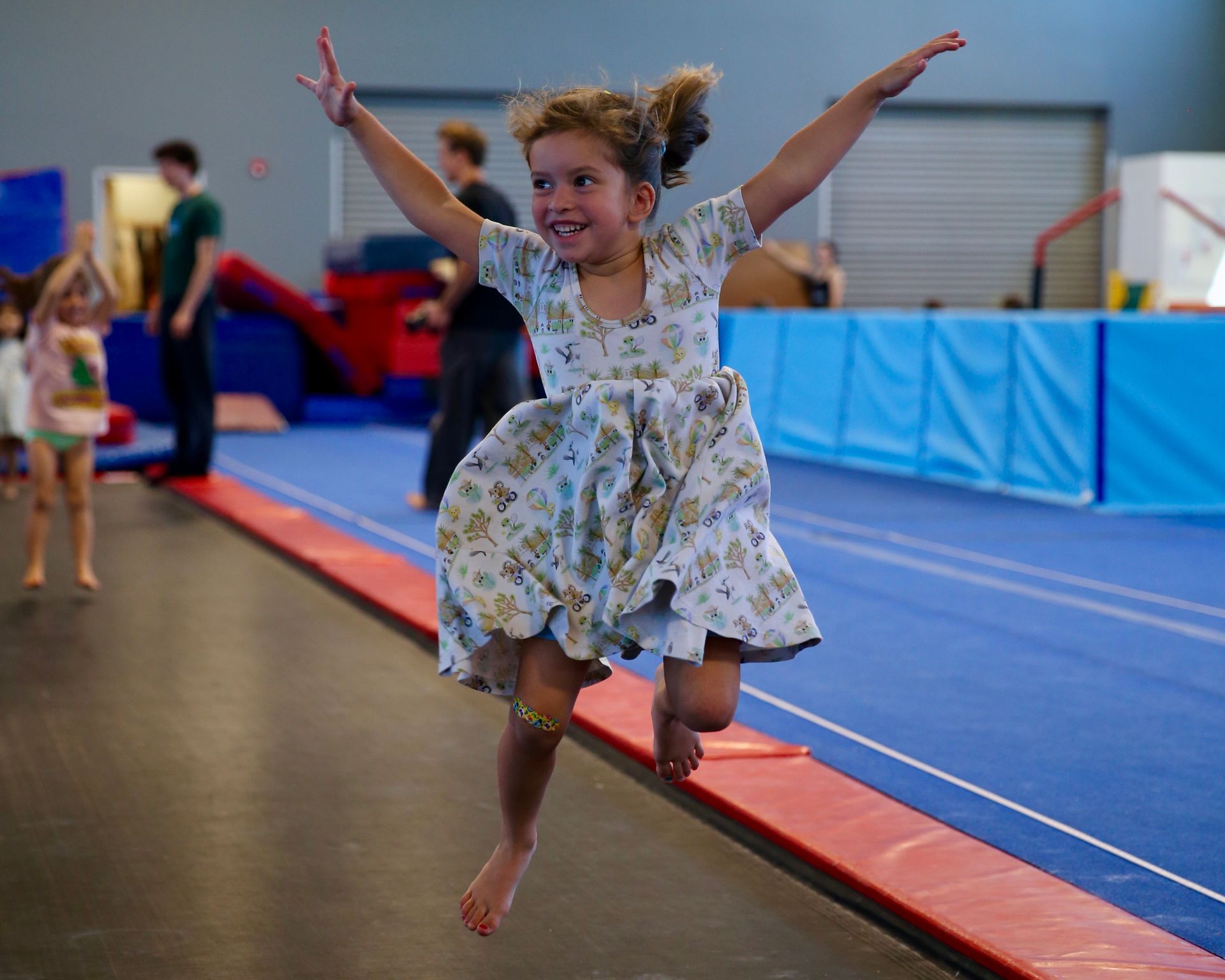 Five smiling children in colorful clothes stretch on a bright studio floor, arms and legs extended.