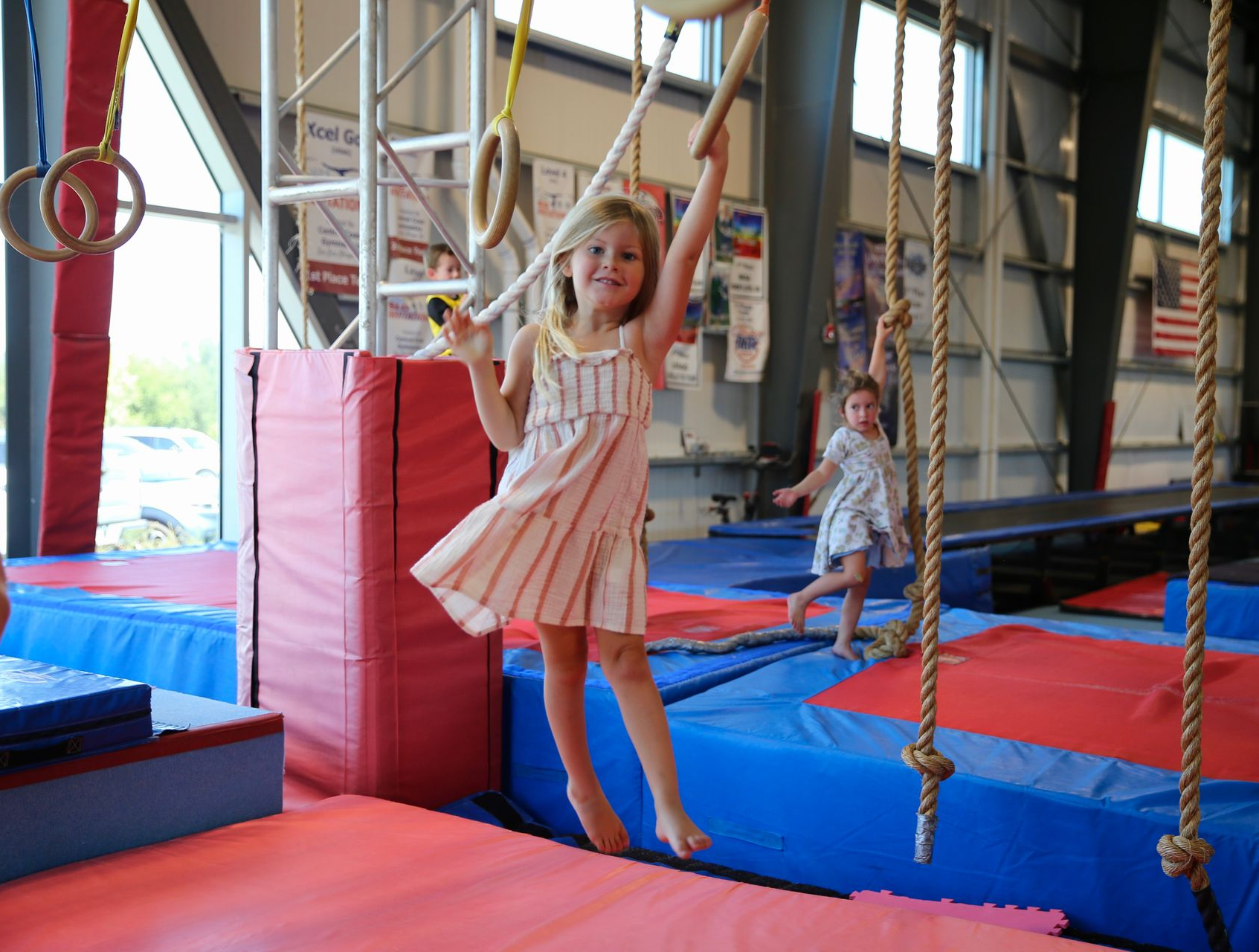 Smiling child in a striped tank top hanging from gym rings indoors