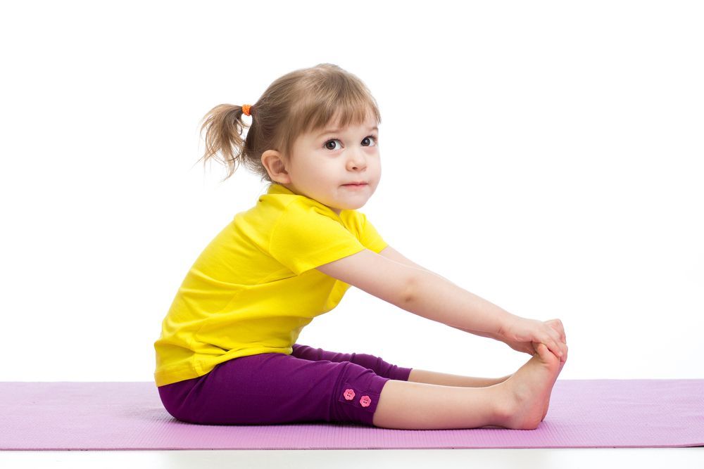 Young cheerleader smiling in a gym, doing a split with pom-poms around her.