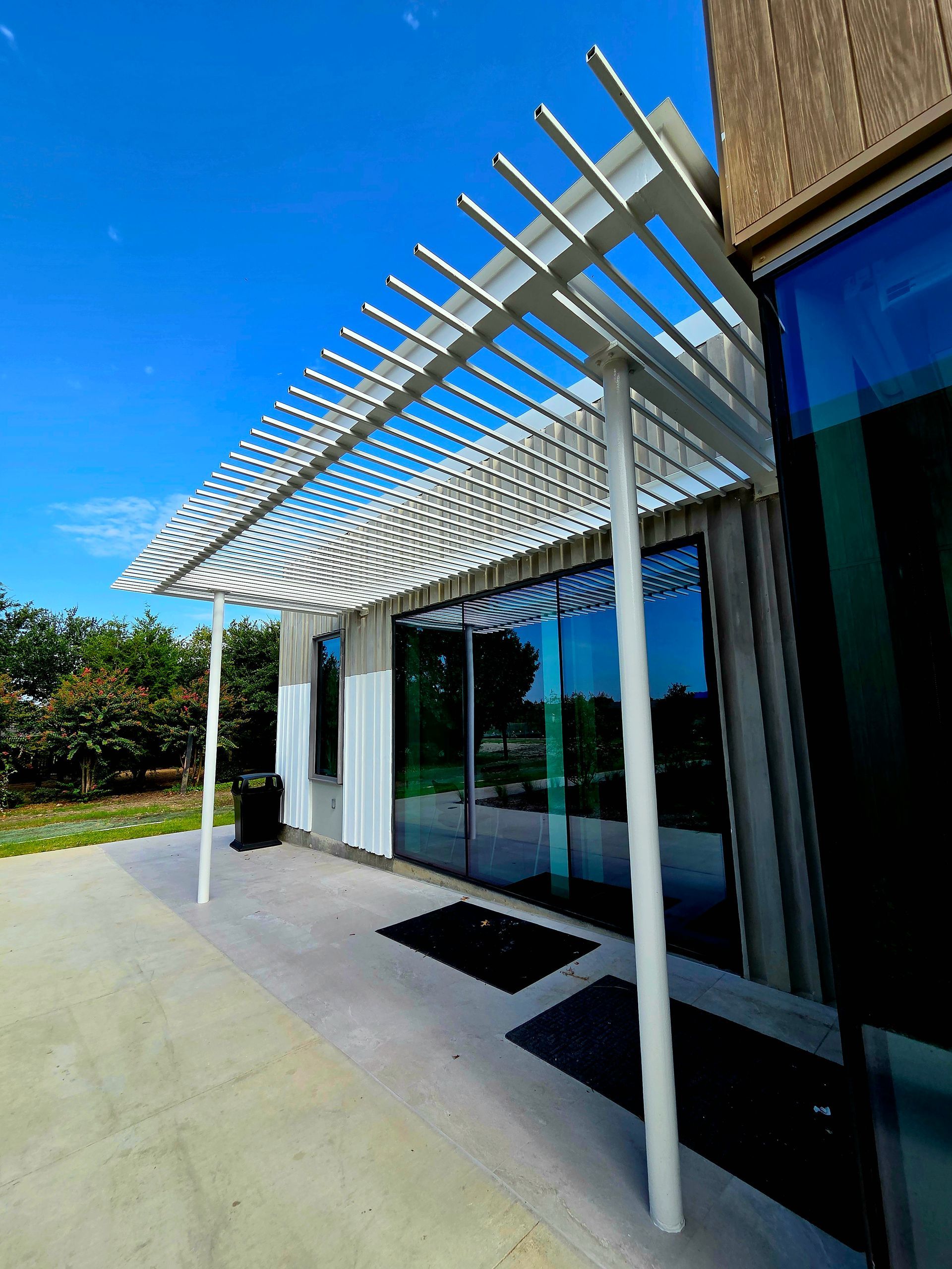 White pergola over a doorway, with glass windows. Bright blue sky overhead.