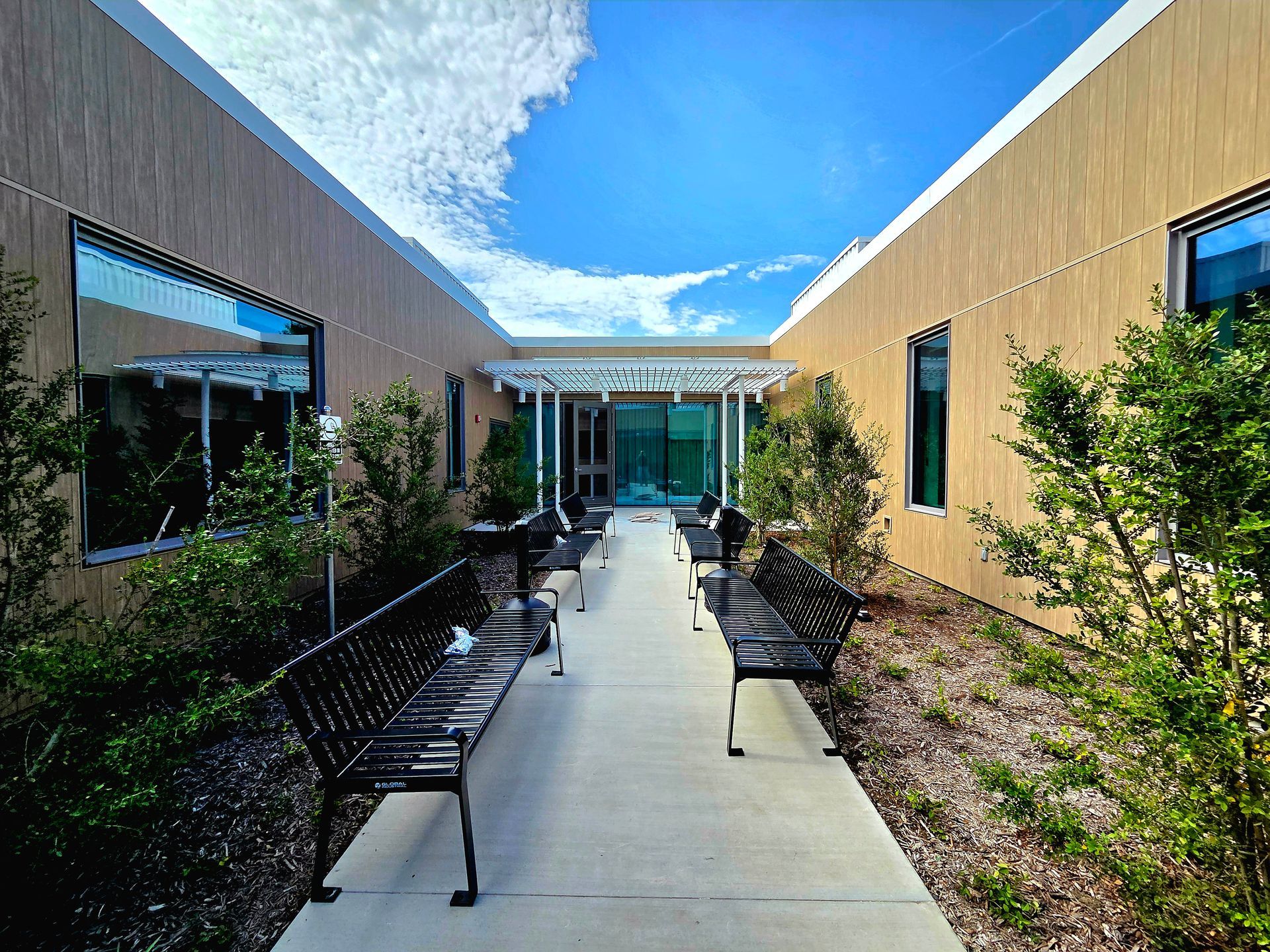 Courtyard between two buildings with benches, greenery, and blue sky.