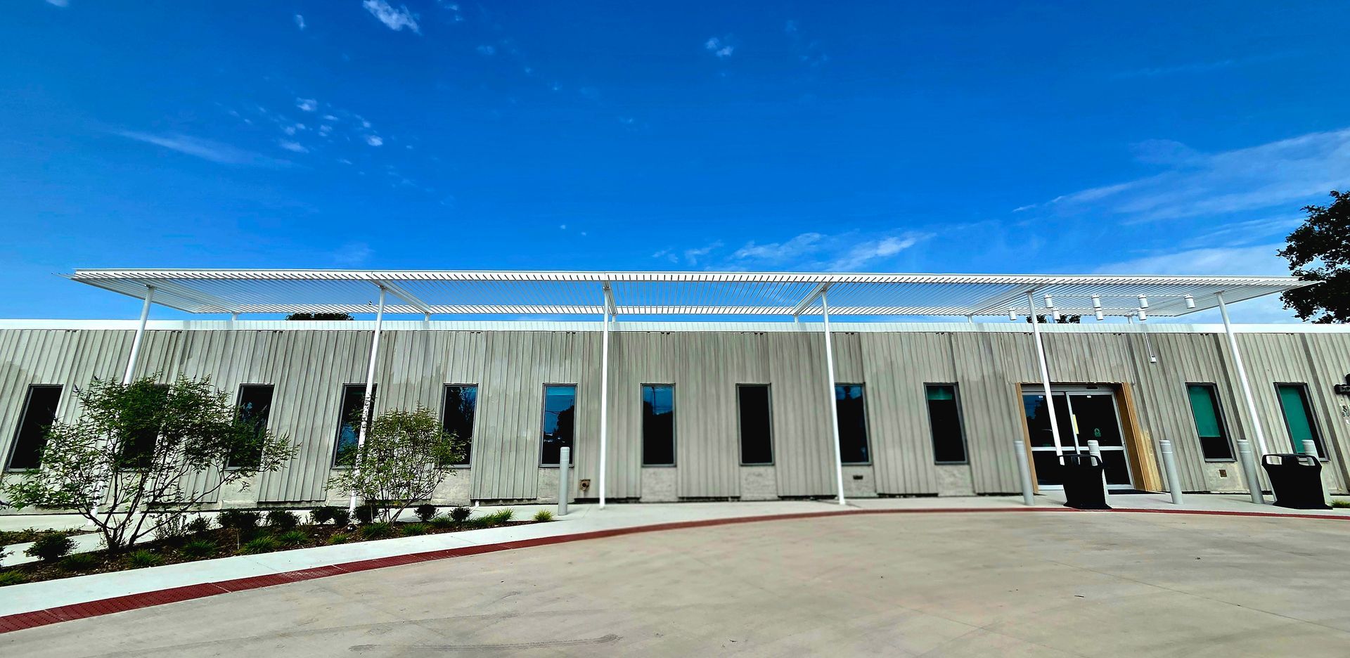 Modern building with a long, white pergola under a bright blue sky.