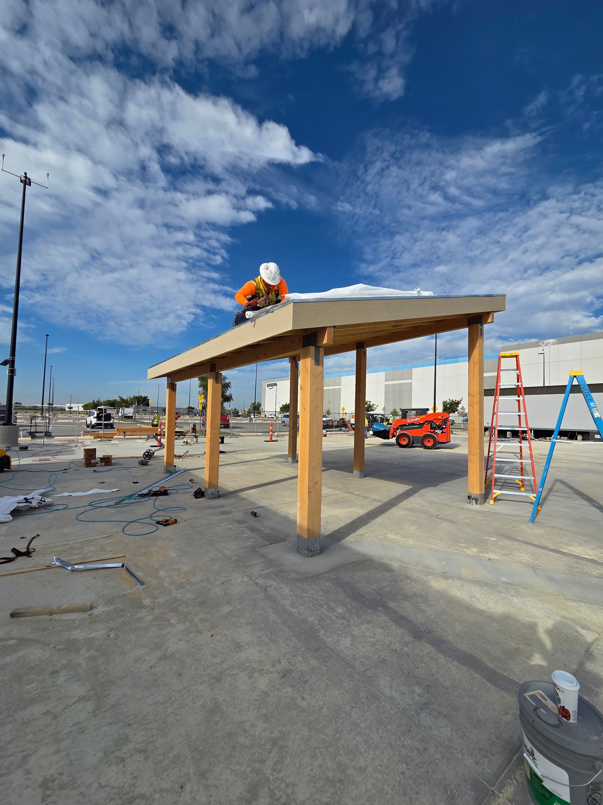 Construction worker on a wooden shelter roof under a blue sky, building site.
