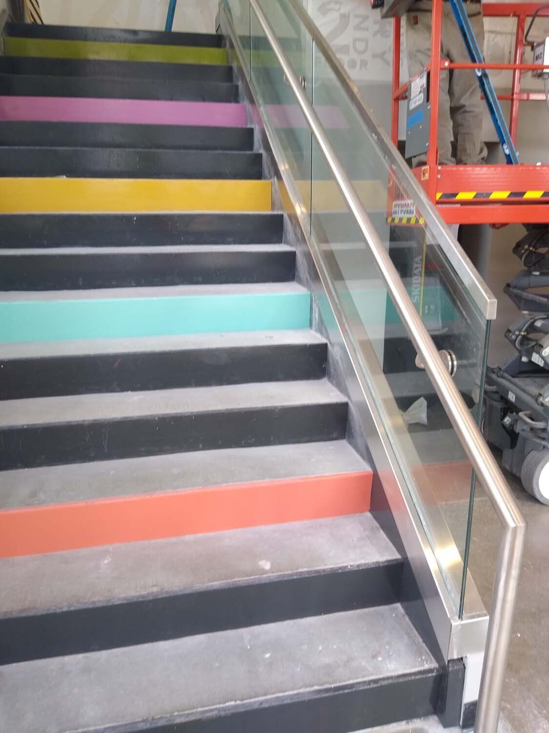 Staircase with colorful risers and glass railing. Metal handrail. A lift in background.