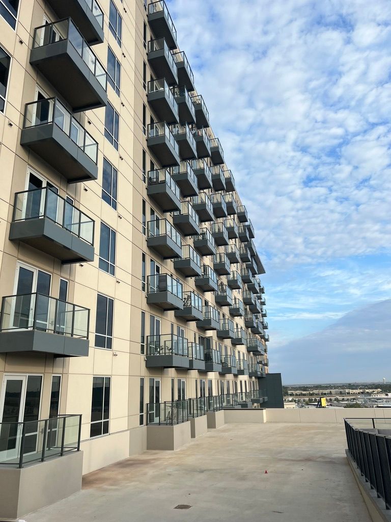 Multi-story apartment building with balconies, beige exterior, and blue sky.