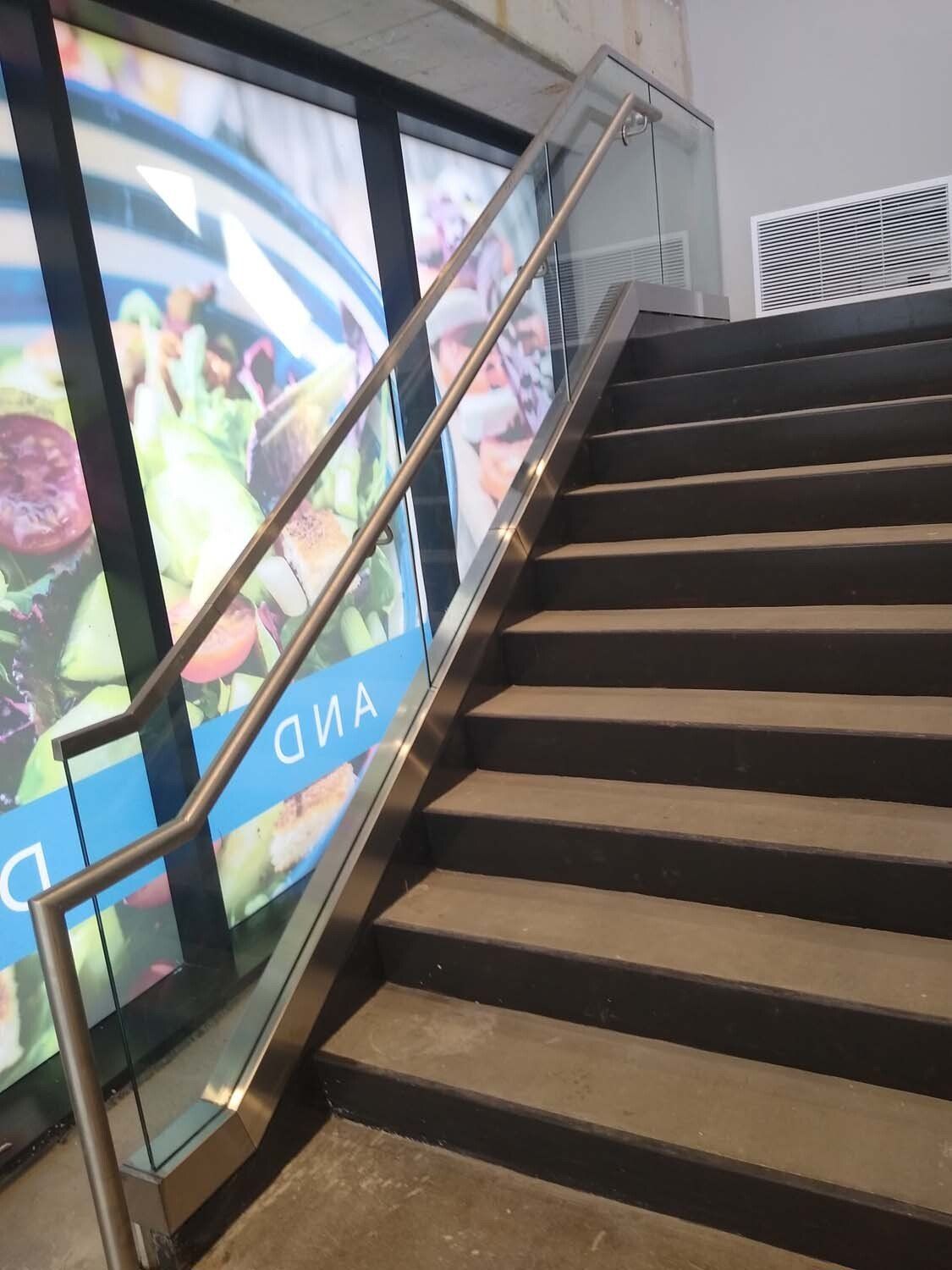 Staircase with stainless steel handrail and glass panel next to a window with colorful advertisement.
