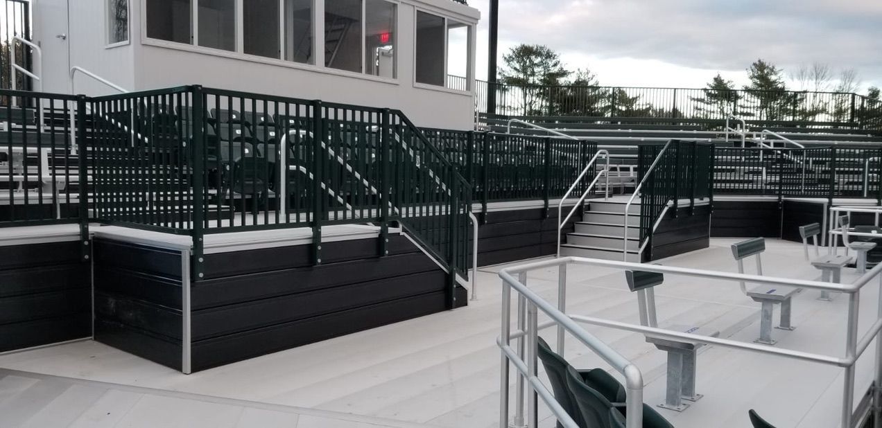 Outdoor stadium seating area with dark green railings and black baseboards.