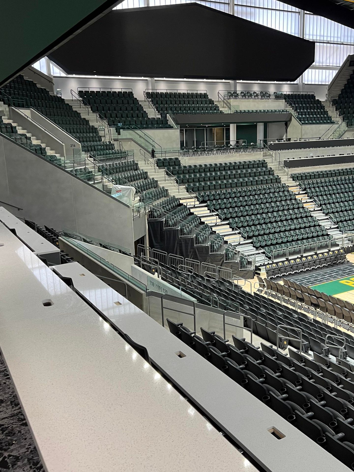 Interior view of a mostly empty arena with green seating and a basketball court below.