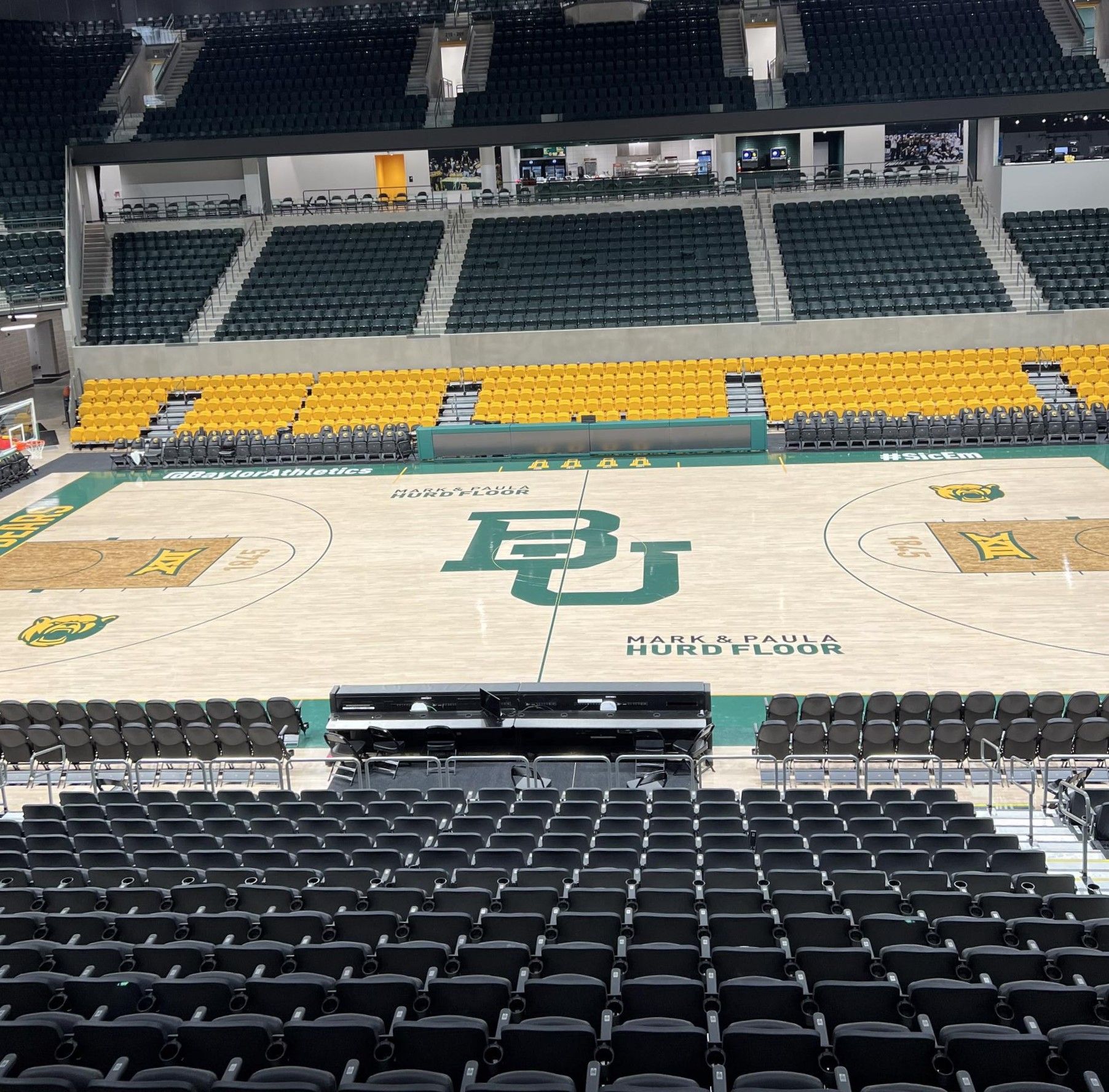 Baylor University basketball court in a green and gold arena. Empty seating surrounds the court.