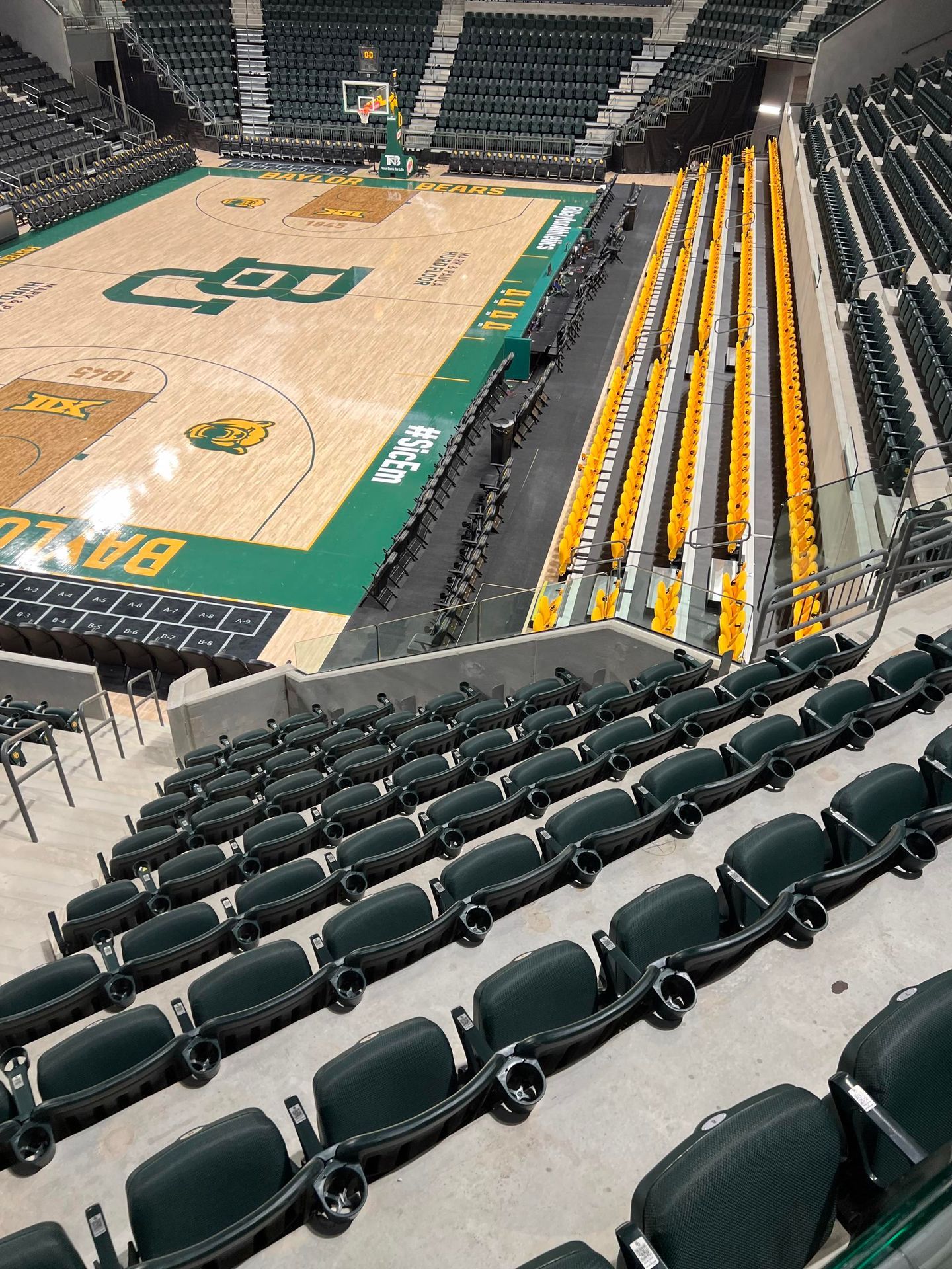 Basketball arena interior: empty green and gold seats facing the court with Baylor branding.