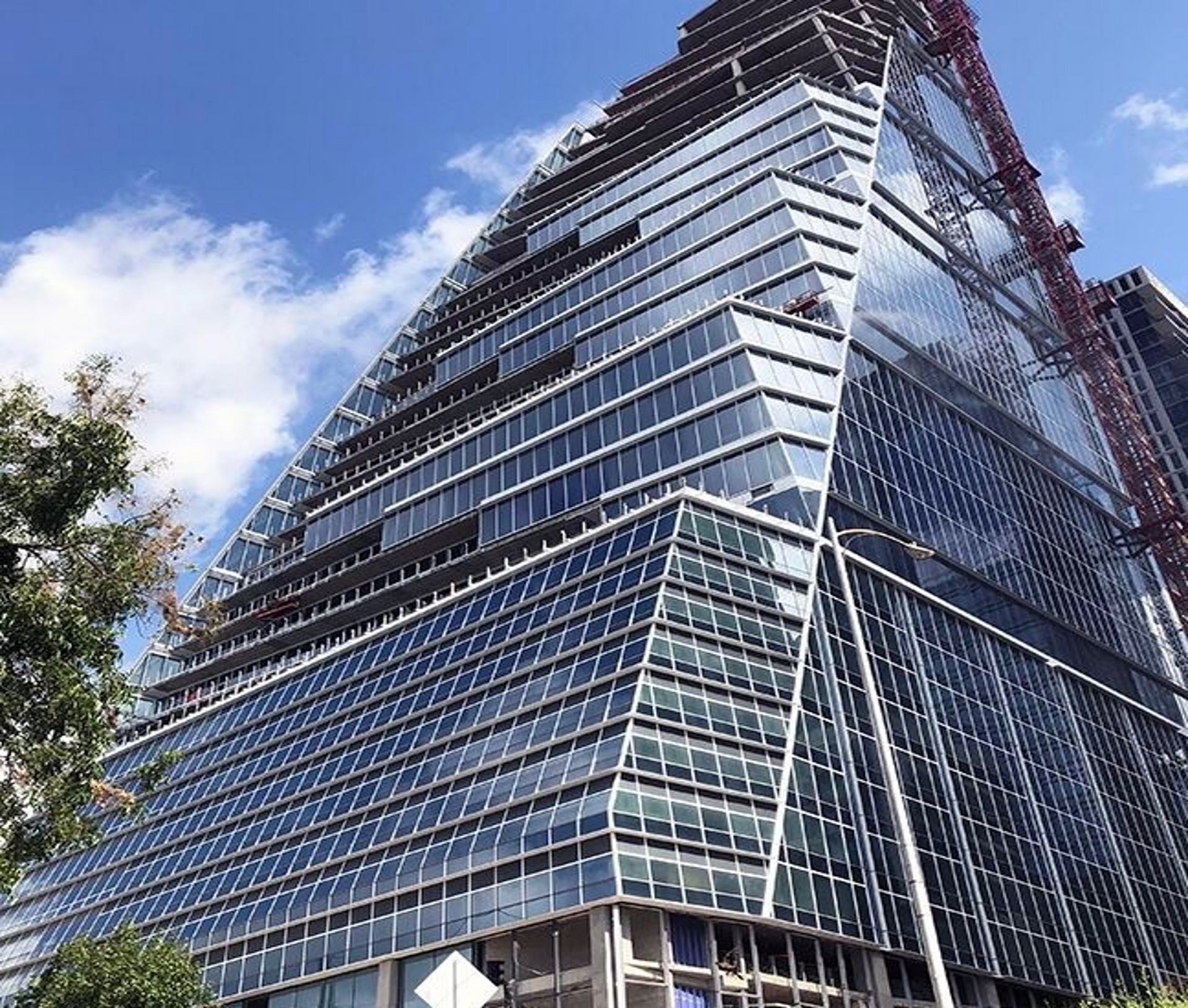 Modern high-rise building under construction with angled glass facade reflecting a blue sky.