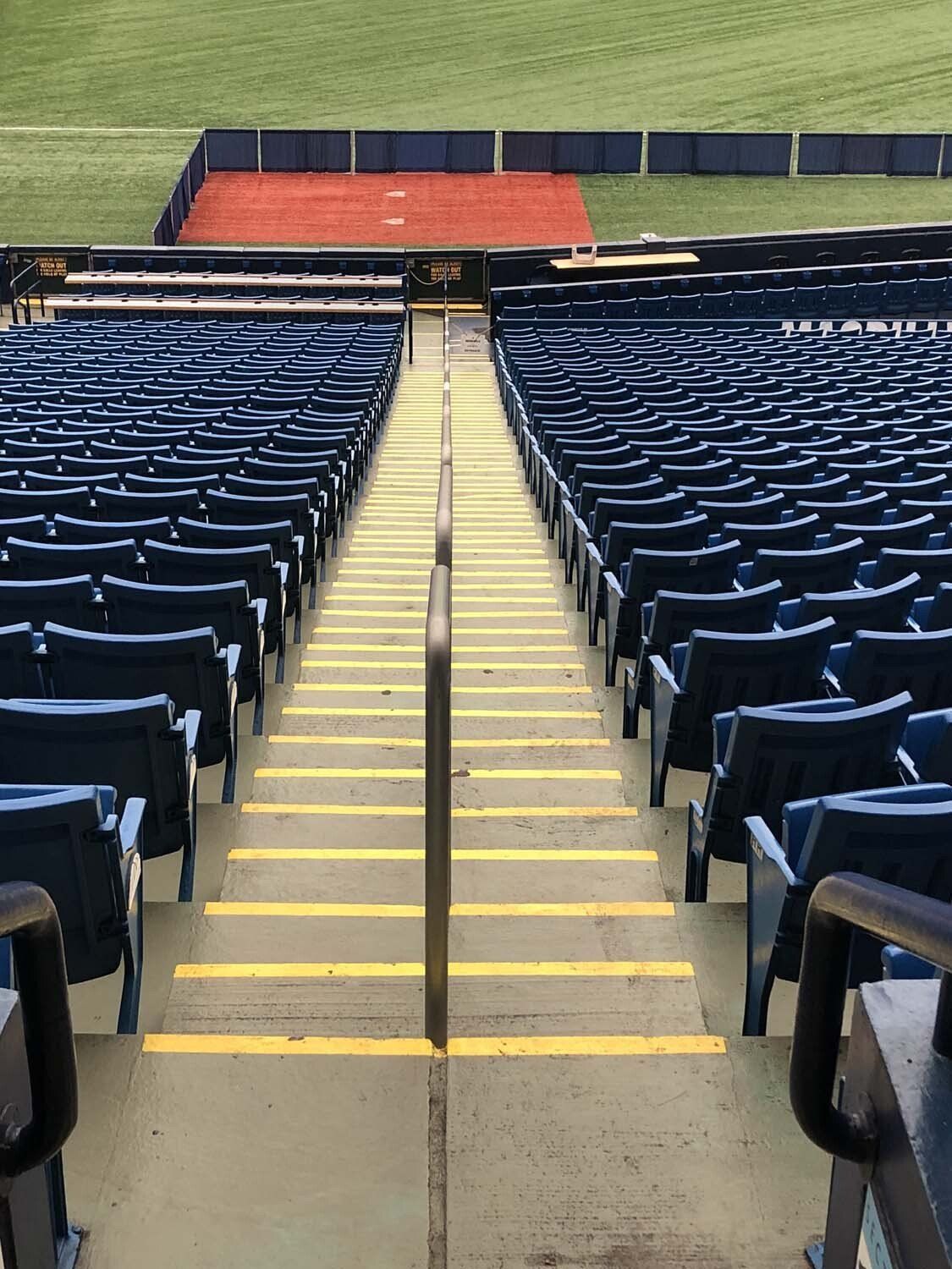Empty stadium seating with central stairway and handrail. Green grass in background.