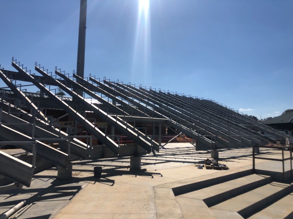 Metal framework of stadium seating under construction outdoors on a sunny day.
