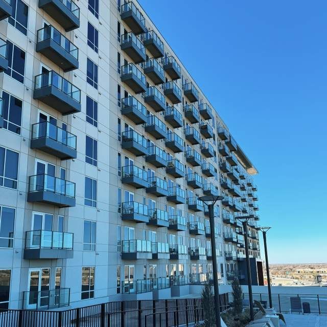 Modern apartment building with many balconies and windows against a clear blue sky.