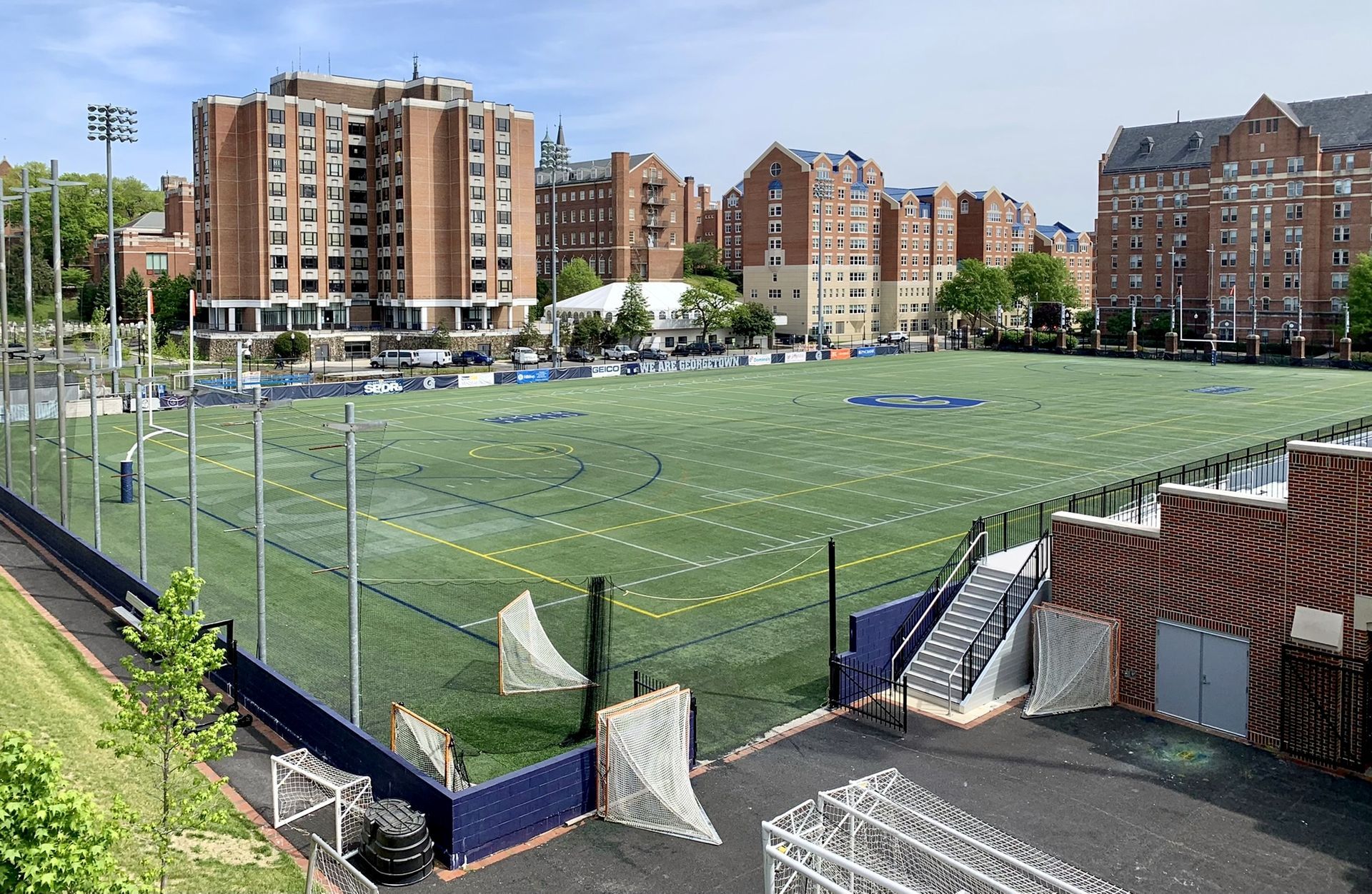 Artificial turf sports field surrounded by brick buildings under a blue sky.