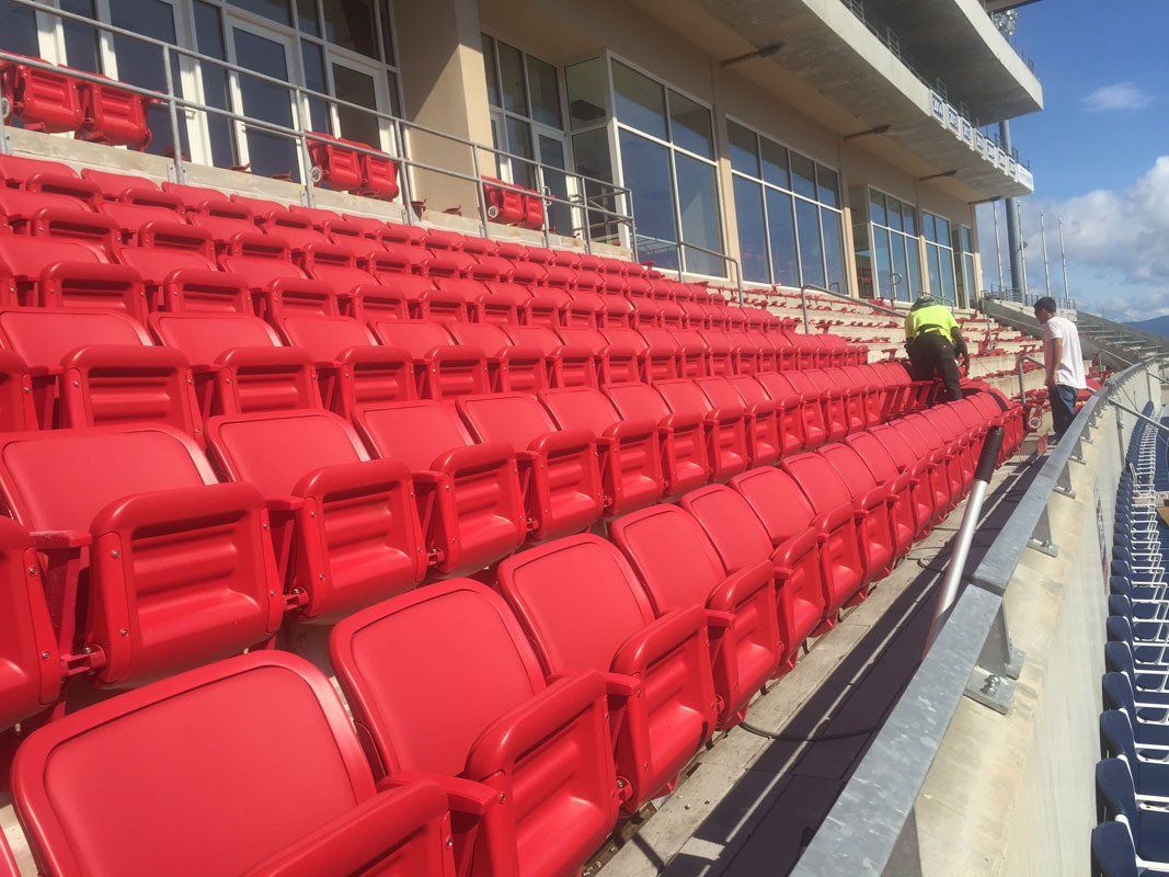 Rows of bright red stadium seats; workers near windowed upper level.