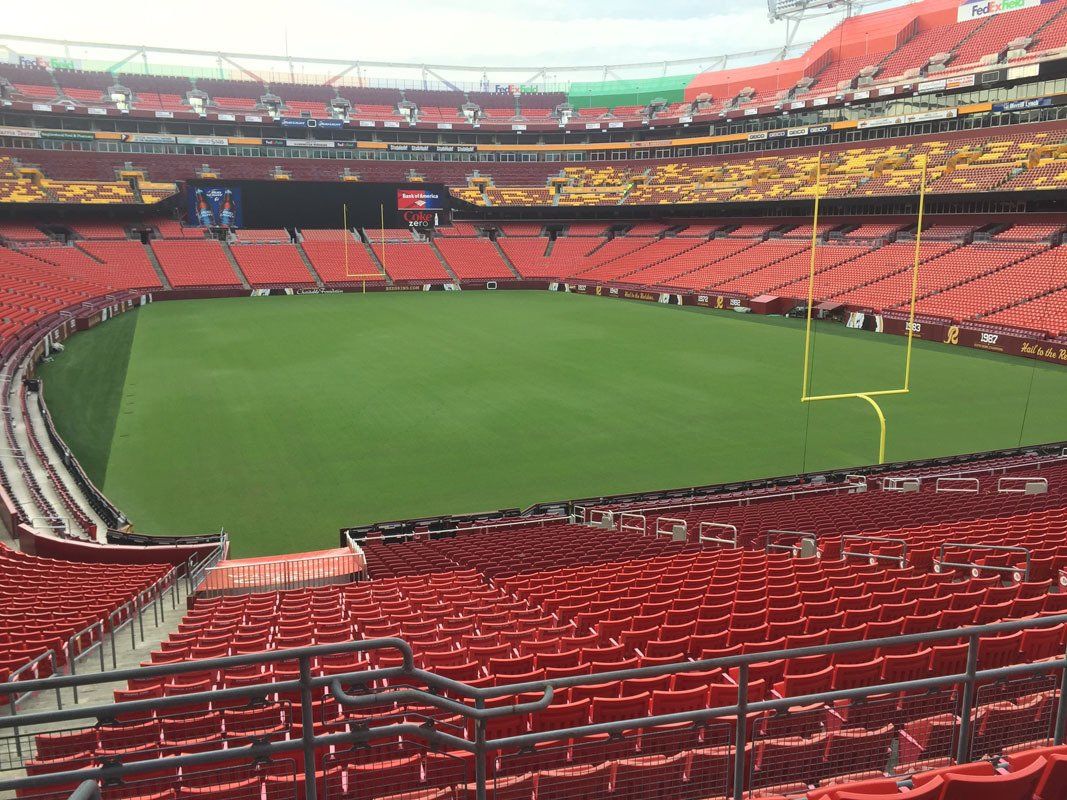 Empty football stadium with red seats, green field, and goalposts.