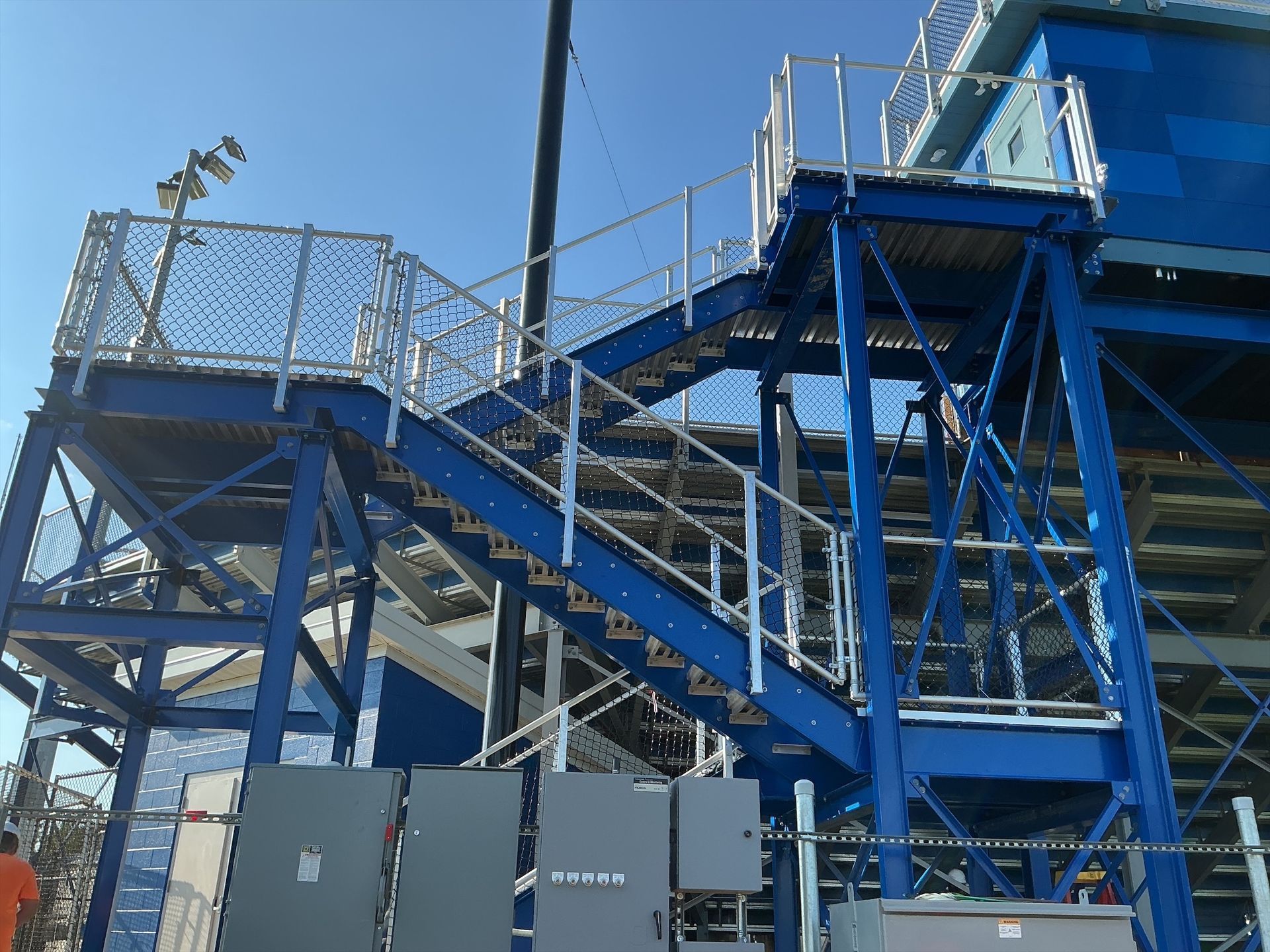 Blue stadium stairs with metal railings, leading to upper seating. Electrical boxes visible.