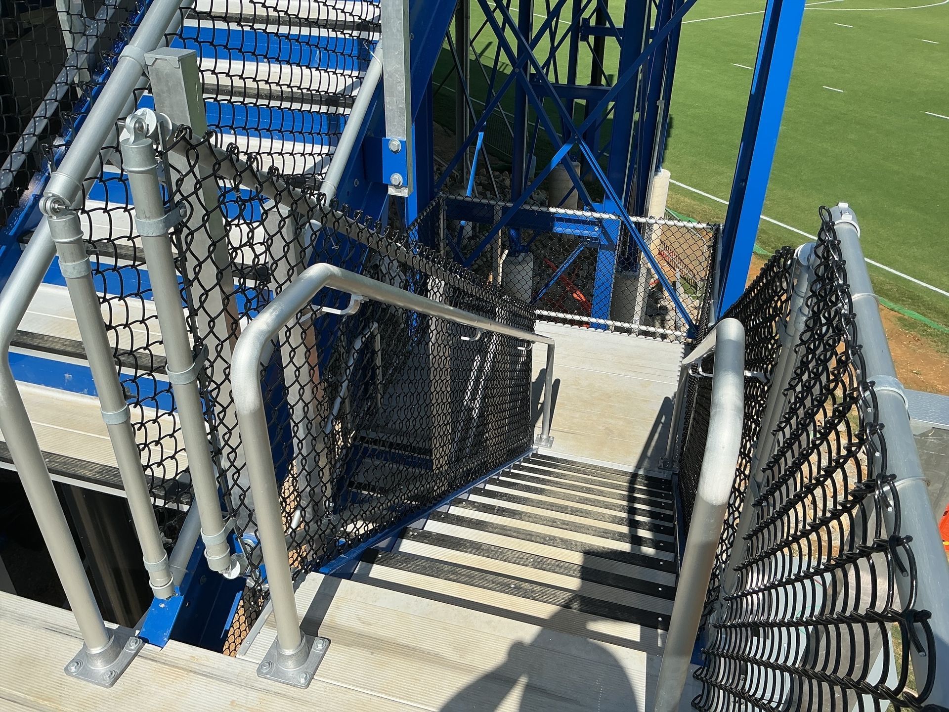 Staircase with metal railings and netting, leading down. Blue tower in the background, set outdoors.
