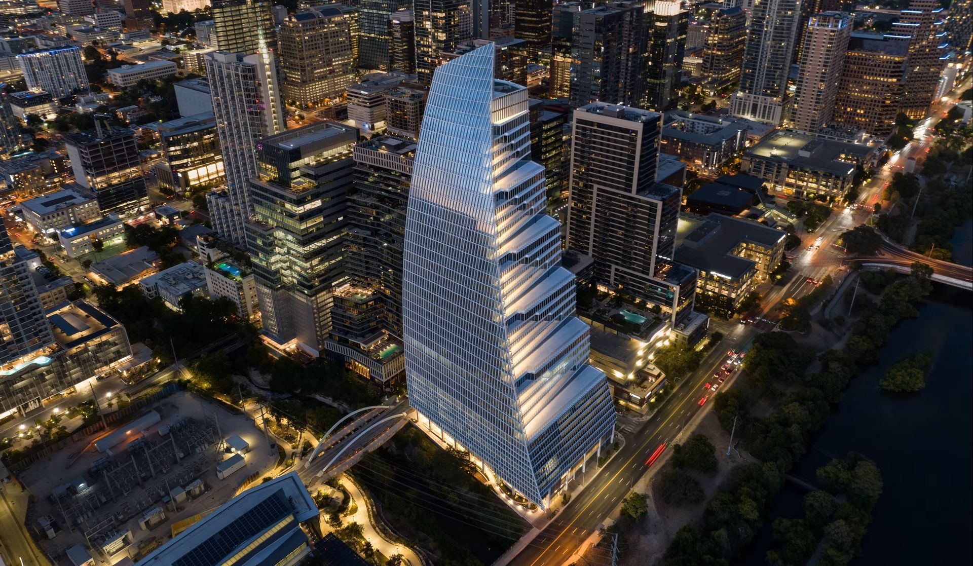 Aerial view of a modern skyscraper at night, with a unique, spiraling design. Buildings and city lights surround it.