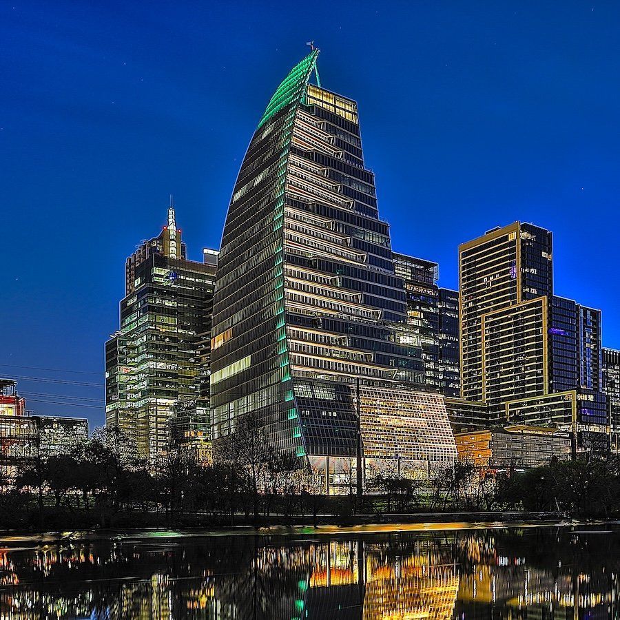 Austin skyline at night with modern skyscrapers reflected in a calm river under a dark blue sky.