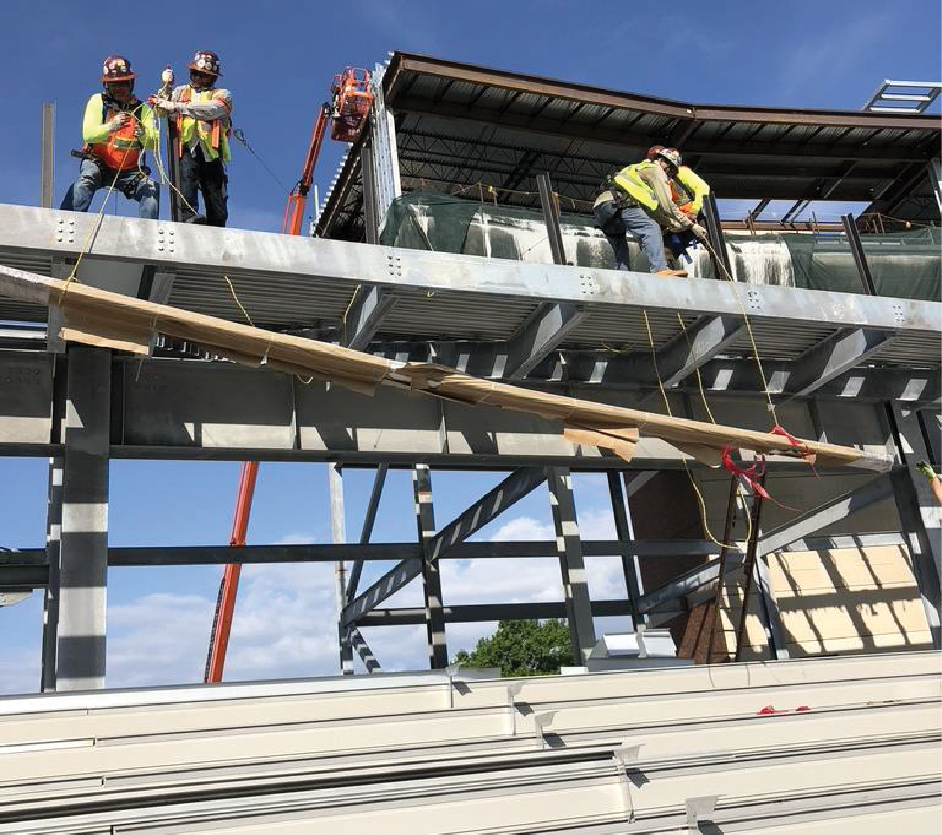 Construction workers installing wooden planks on a metal framework; orange crane and blue sky background.