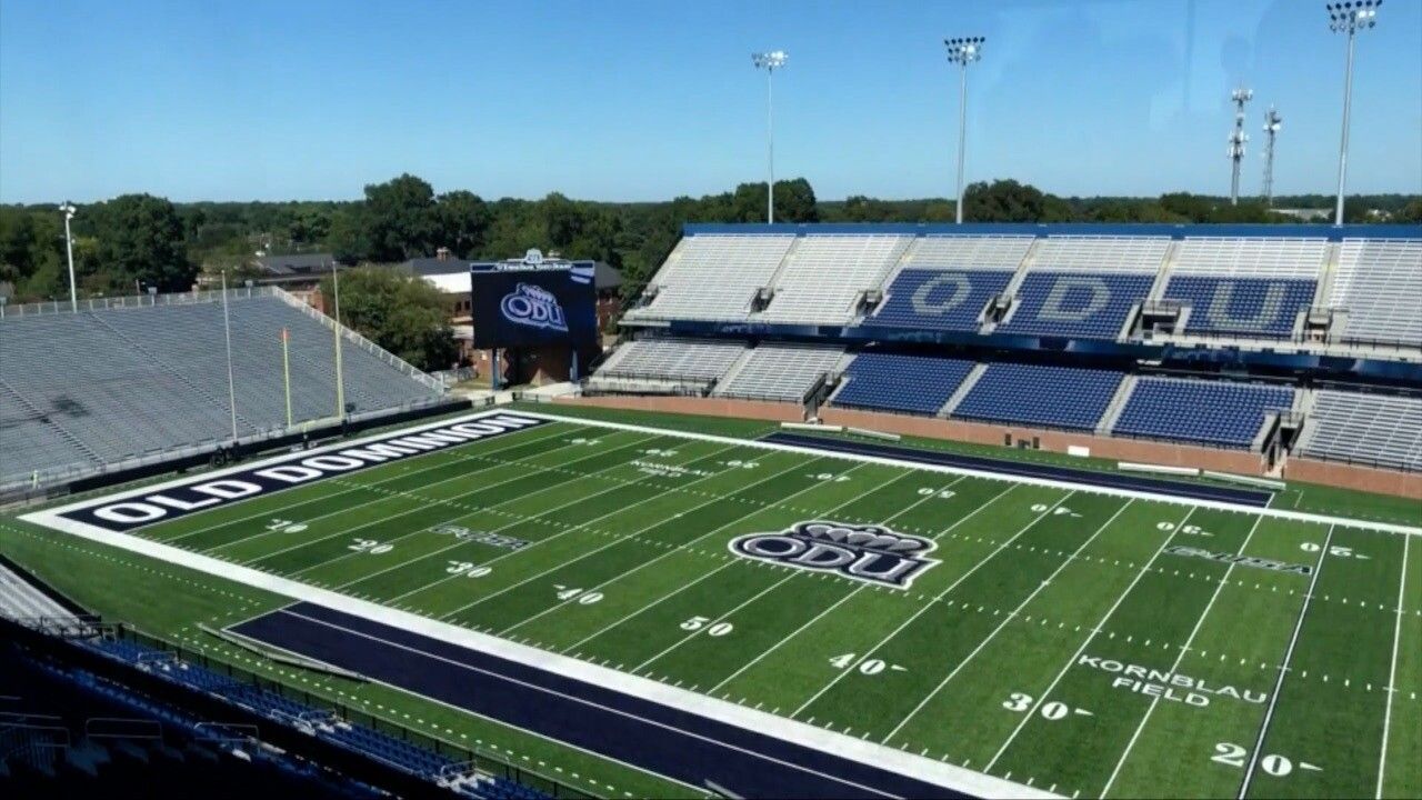 Football field at ODU stadium, sunny day. Blue and white seating, green field with ODU logo.