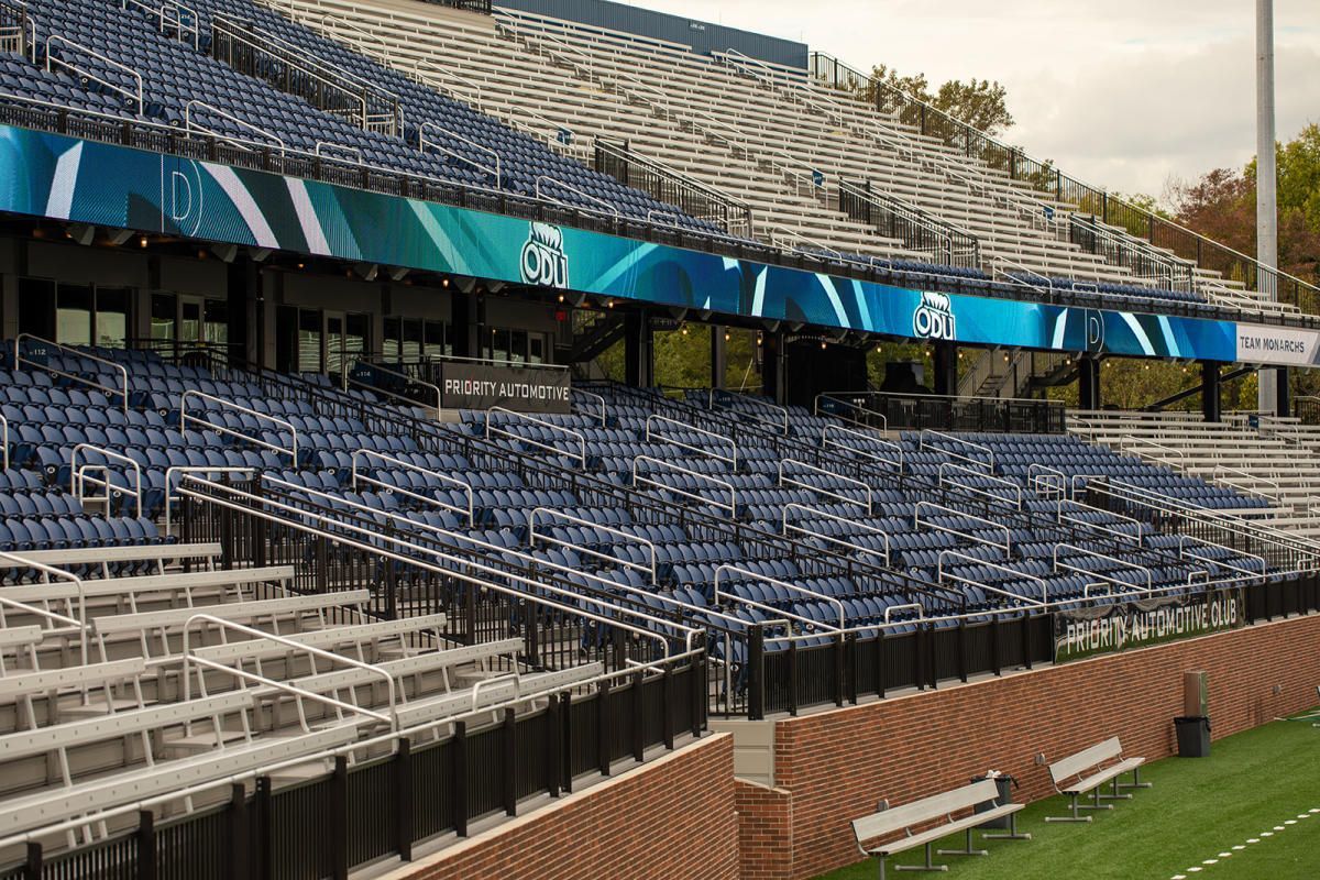 Empty stadium seating with blue chairs, blue and white signage, and brick walls.