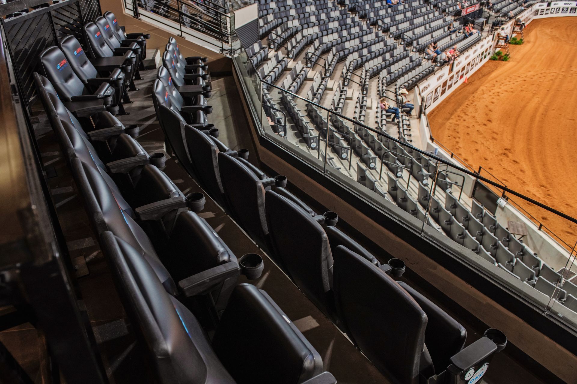 Empty stadium seating overlooking a rodeo arena with dirt floor and metal railing.