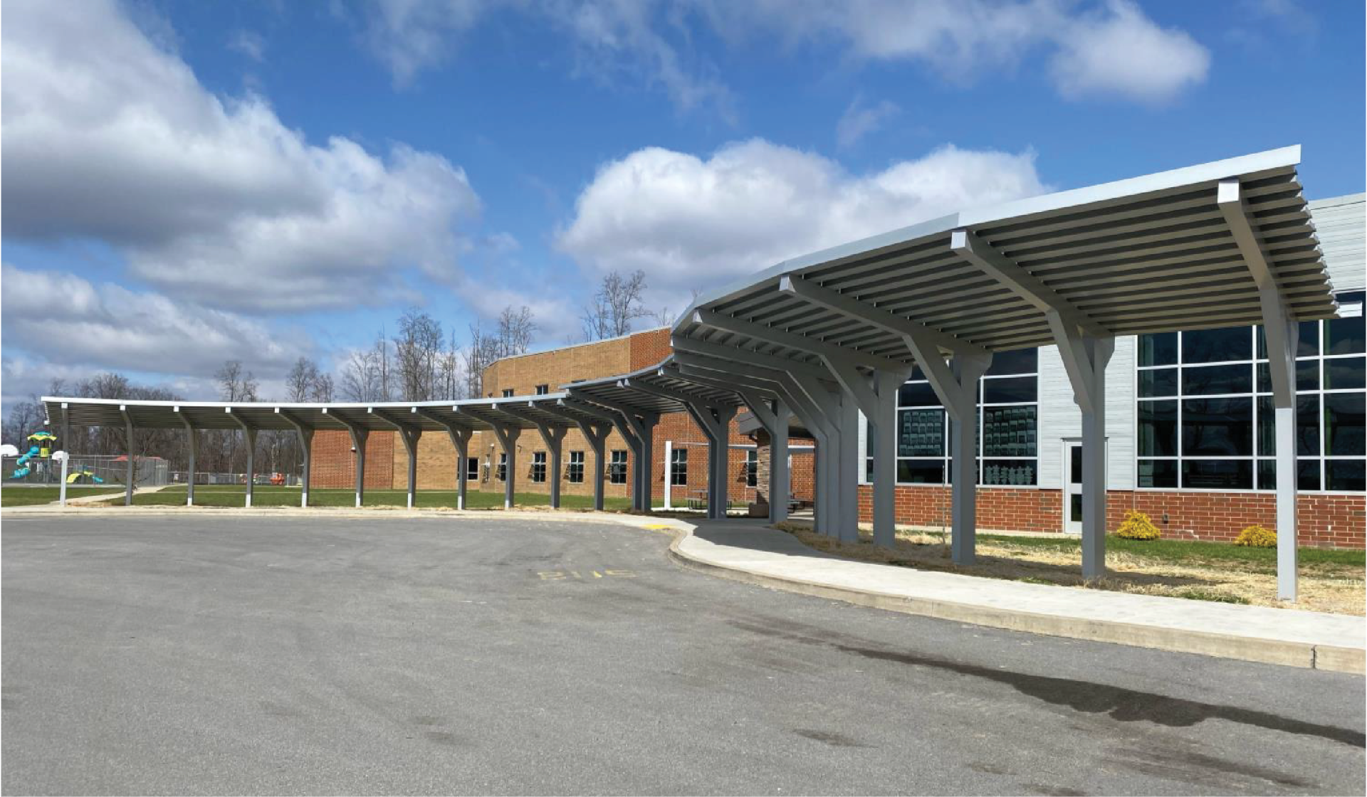 Covered walkway at a building entrance; gray canopy, brick walls, and clear sky with clouds.