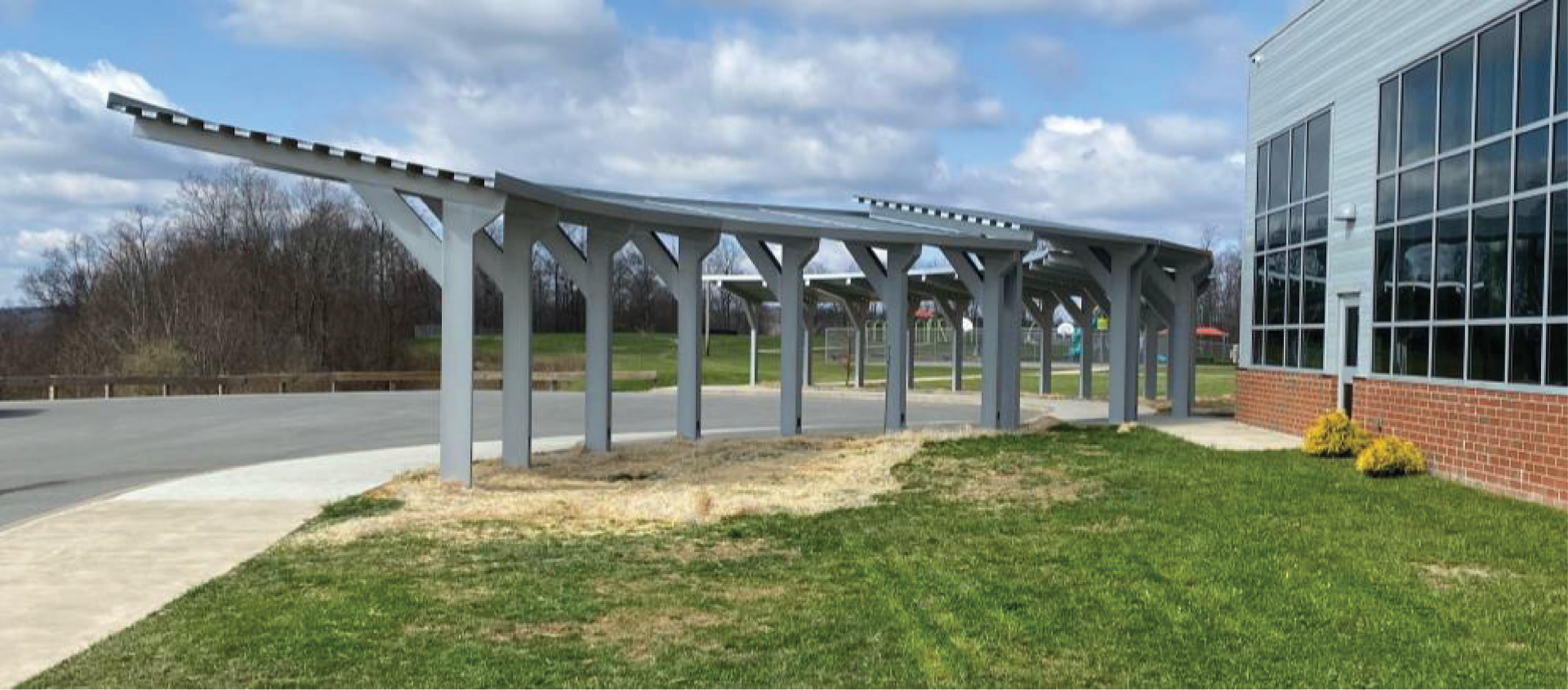 Covered walkway with a building on the right and grass on the lower right, the sky is cloudy.