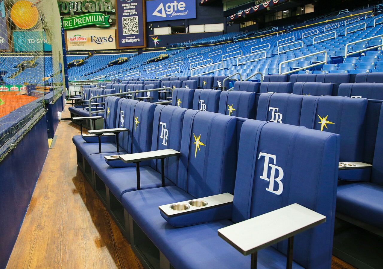 Rows of blue stadium seating with small tables and Tampa Bay Rays logo, in a baseball stadium.