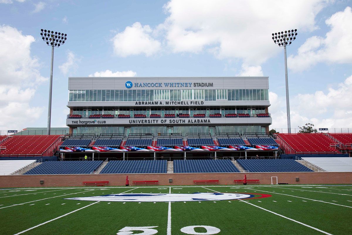 Football stadium with blue seats, red accents, and a white press box under a cloudy sky.