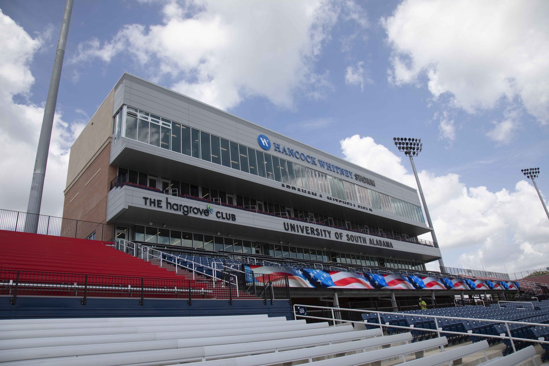Football stadium exterior with red and blue seating and a sky with clouds.