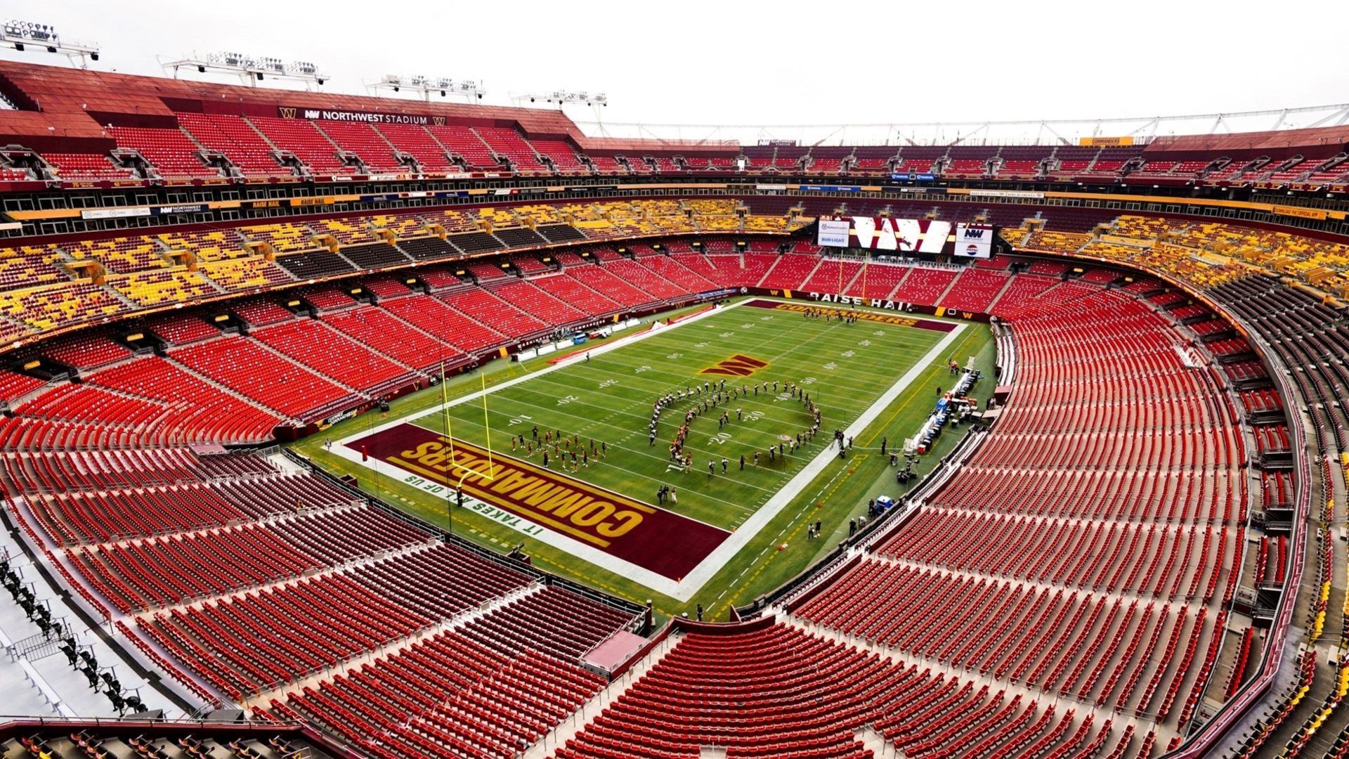 Empty football stadium, red and yellow seating, green field with marching band.