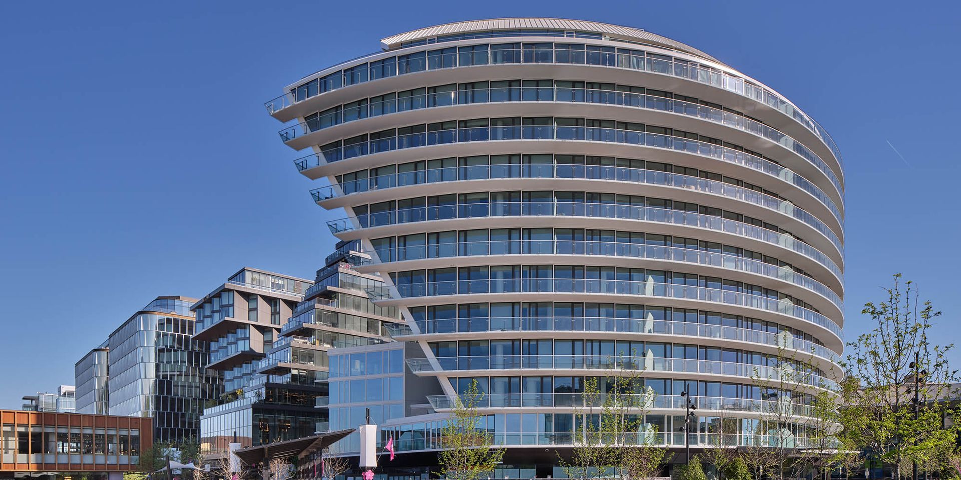 Modern curved building with balconies, blue sky in background.